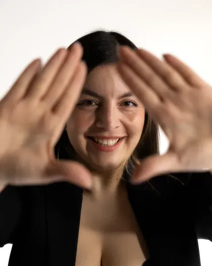 Retrato de marca personal en estudio: mujer sonríe entre sus manos abiertas, primer plano en fondo claro