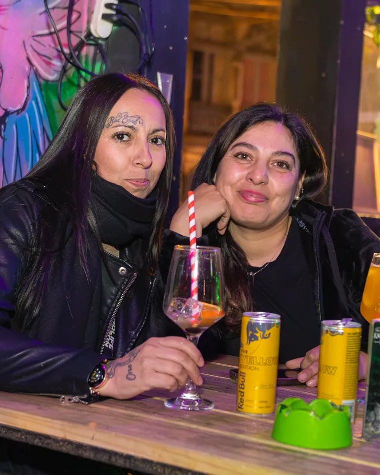 Dos mujeres posando junto a su trago y un mural de colores, cobertura de noche para un bar de Valparaíso