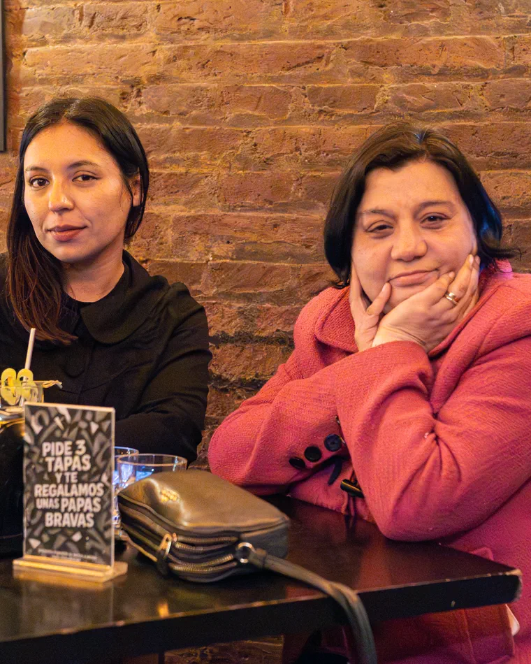 Dos mujeres sentadas a la mesa frente al muro de ladrillos, contenido mensual para un bar de Valparaíso