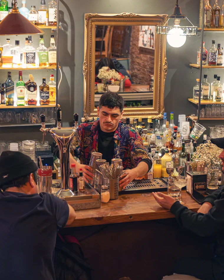 Barra iluminada con las botellas al fondo mientras el bartender atiende, fotografía de bares en Valparaíso