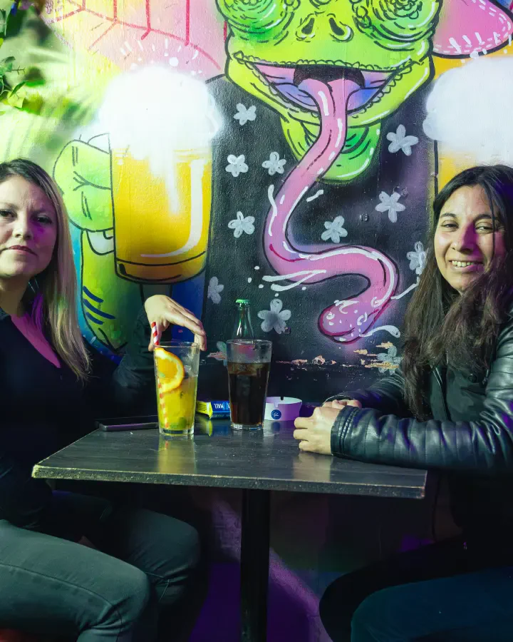 Dos mujeres con sus bebidas en una mesa de bar frente a un mural, pack mensual de contenido en Valparaíso