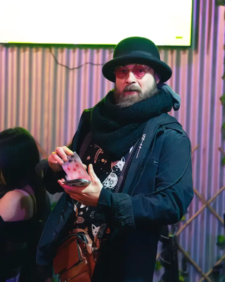 Hombre de sombrero y lentes redondos con su celular bajo luz lila, para pack mensual de contenido