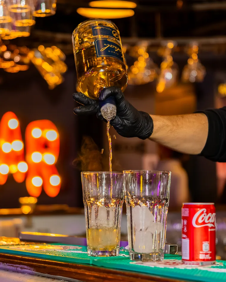 Destilado servido en dos vasos con hielo sobre la barra, fotografía gastronómica en un bar de Valparaíso