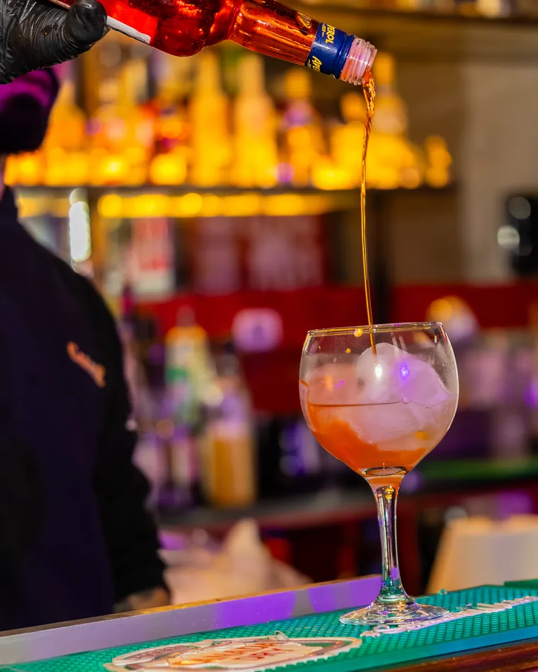 Copa balón con hielo recibiendo un licor rojo desde la botella, fotografía gastronómica en Valparaíso