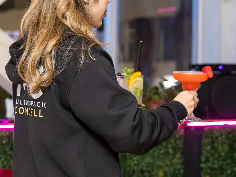 Alguien de espaldas alza una copa margarita naranja en la terraza, cobertura de noche en un bar de Valparaíso