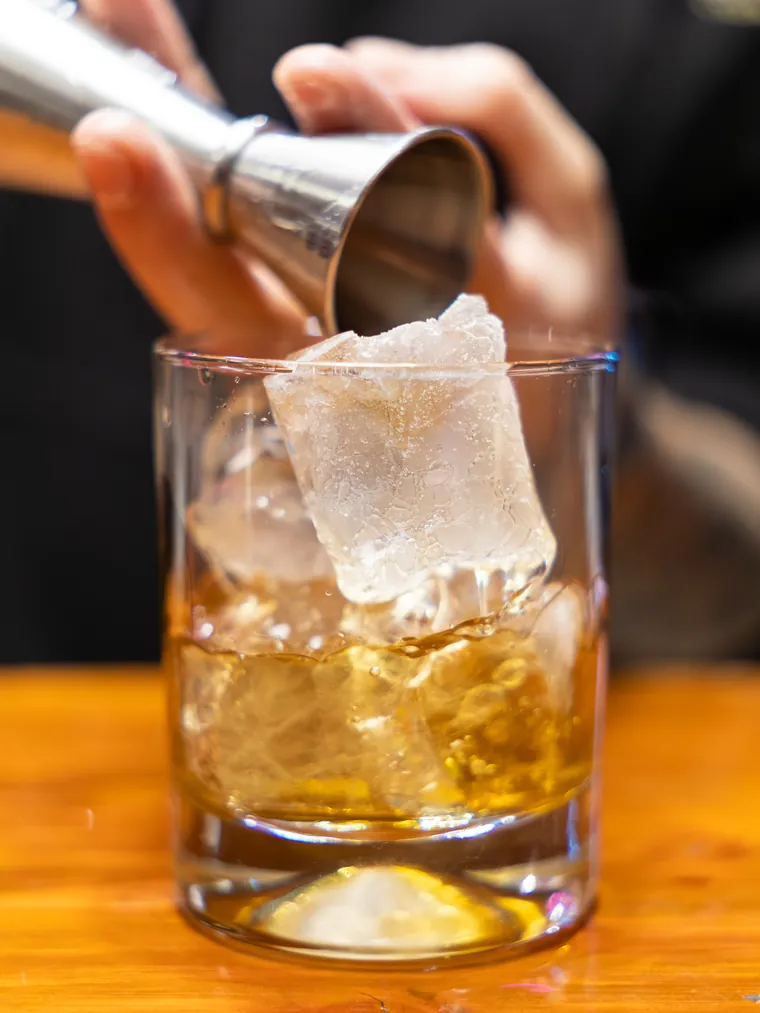 Medida de licor cayendo sobre el hielo del vaso, cuadro del video de coctelería