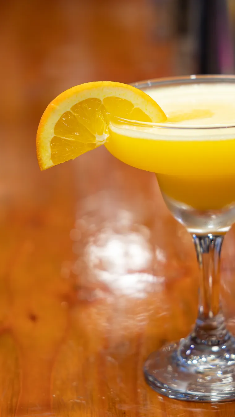 Copa con trago amarillo y rodaja de naranja en la barra de madera, fotografía de tragos en Valparaíso
