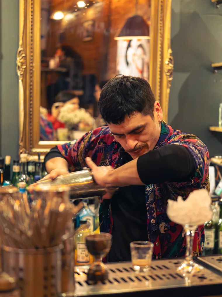 Bartender agitando la coctelera junto a una copa coronada con algodón de azúcar, fotografía gastronómica