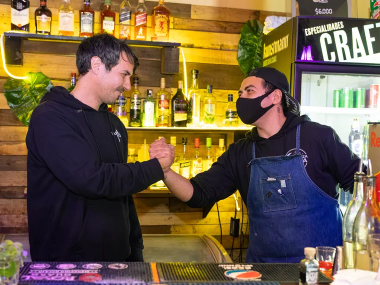 Dos bartenders saludándose tras la barra de un bar de Valparaíso, cobertura del local