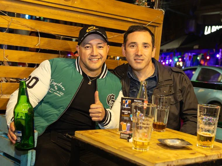 Dos hombres brindando con sus cervezas en la mesa de un bar de Valparaíso, cobertura de noche