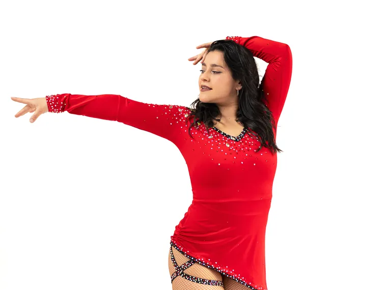 Bailarina de vestido rojo con brillos extiende un brazo en estudio de fondo blanco, fotografía de danza