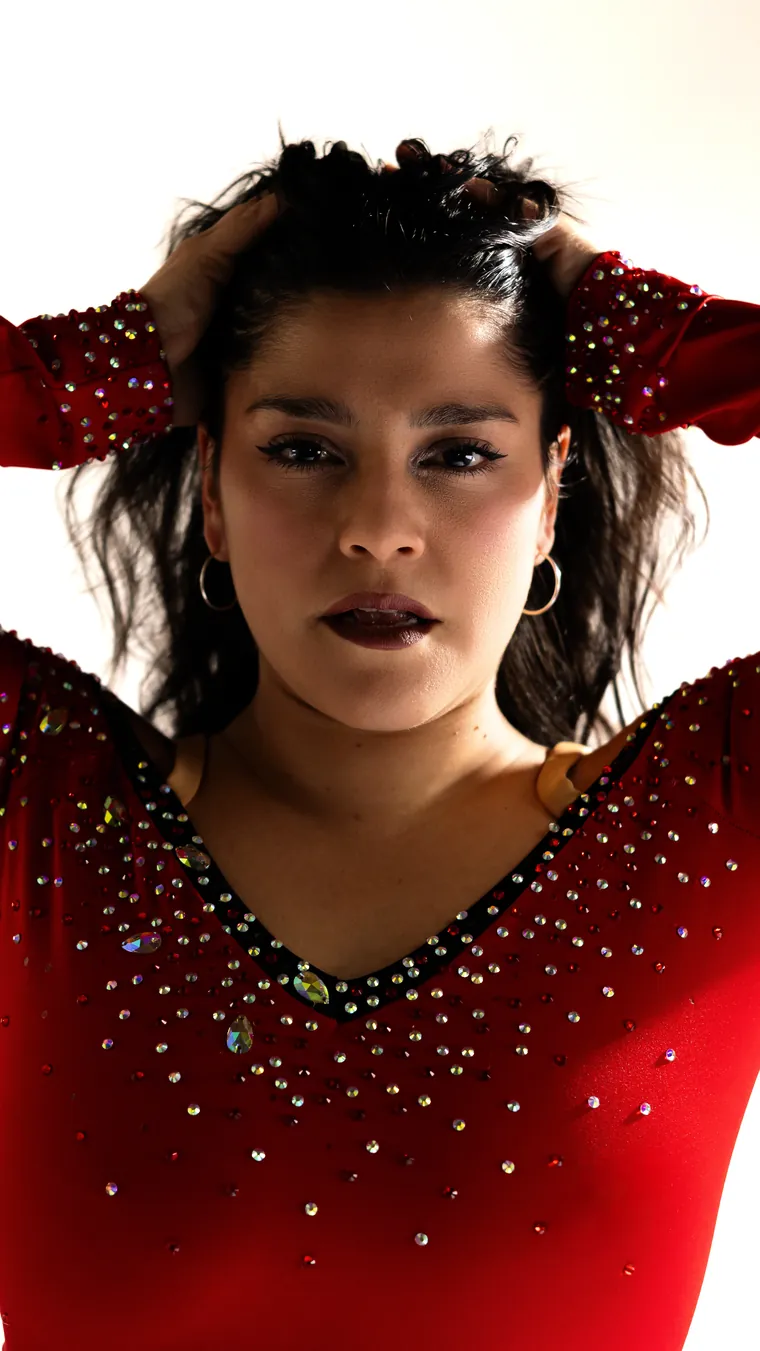 Primer plano de bailarina con las manos en el pelo y vestido rojo con pedrería, fotografía de danza