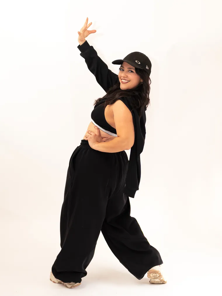 Bailarina urbana de jockey negro alza el brazo y sonríe en estudio, fotografía de danza en Valparaíso