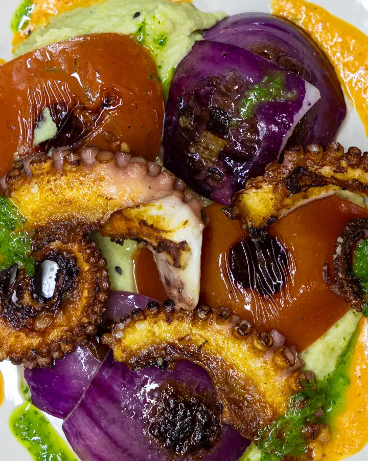 Tentáculos de pulpo dorados con cebolla morada asada y salsas verde y naranja, fotografía gastronómica