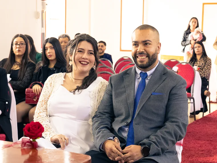 Los novios ríen sentados durante la ceremonia, con los invitados detrás