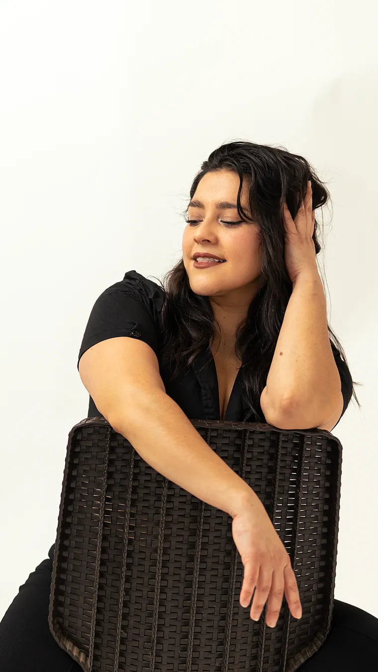 Retrato de estudio: mujer apoyada en una silla de mimbre, con la mano en el pelo